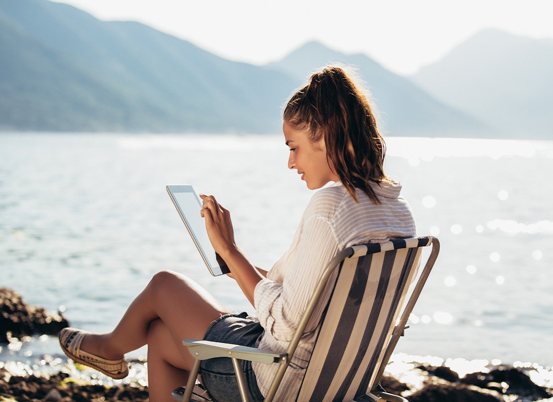Video Library - Smiling Woman Sitting on Deck Chair by the Sea Using Tablet on a Sunny Day