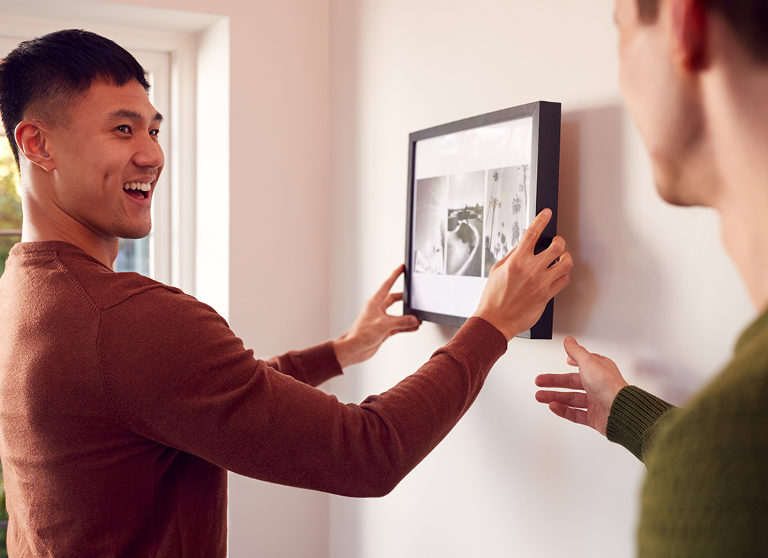 Assurant Renters Insurance - Man Smiling While Hanging a Photo at Their Apartment Next to a Window